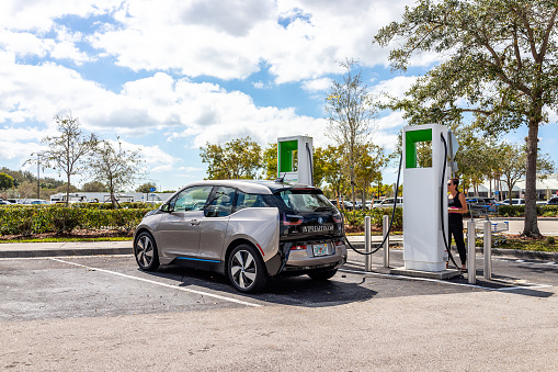 Naples, USA - March 1, 2022: Electrify America EV electric vehicle charger station with woman paying for BMW eDrive car charging in Florida