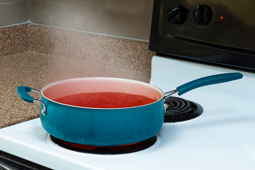 Horizontal shot of a blue pot on a stove top holding steaming tomato soup.