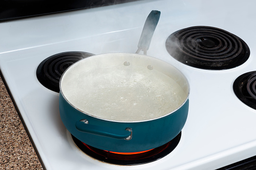Horizontal shot of a blue pot on a stove top holding boiling water with steam rising.