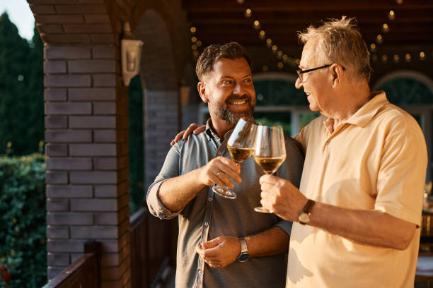 Happy man and his senior father toasting with wine after family lunch on a patio. Happy senior man and his son toasting with wine during family gather on a terrace. father in law stock pictures, royalty-free photos & images