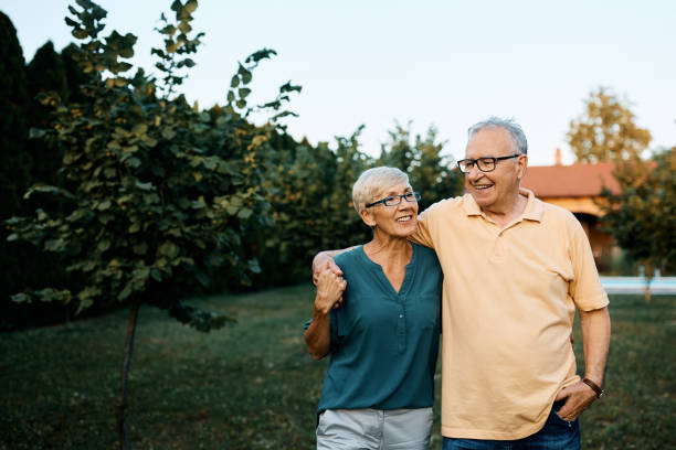 Embraced senior couple walking through their backyard. Happy senior couple enjoying while walking embraced in their backyard. Copy space. senior couple stock pictures, royalty-free photos & images