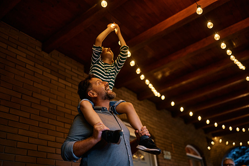 Happy father carrying his son on his shoulders while turning on the lightbulb on a patio.