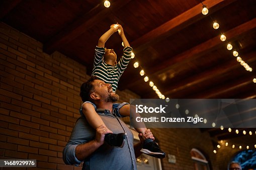 istock Little boy turning on the light bulb while father is holding him on his shoulders on a terrace. 1468929976