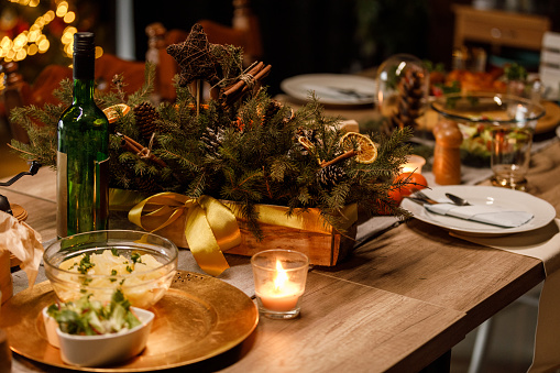 Close up shot of rustic set up on a dining table for a Christmas dinner party. Tea candles, beautiful center piece and salads served next to a bottle of wine.