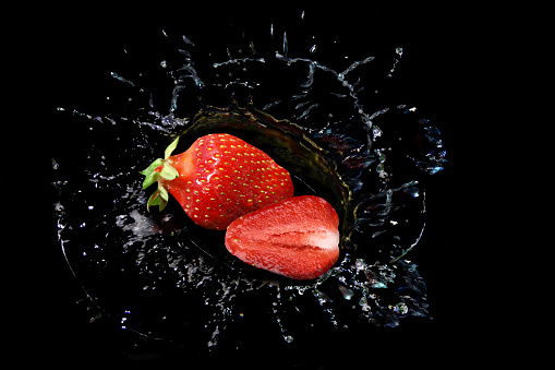 Strawberries dropped into water on a black background.