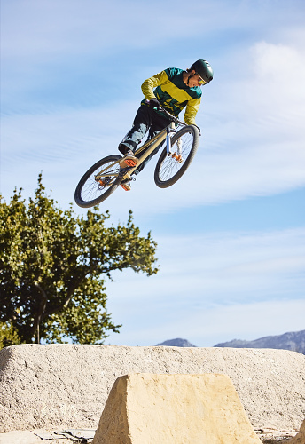 Man, cyclist and mountain biking in free style, tricks or extreme hill jumping in the nature outdoors. Professional male cycling in the mountain with bicycle in the air for freedom, parkour or sports