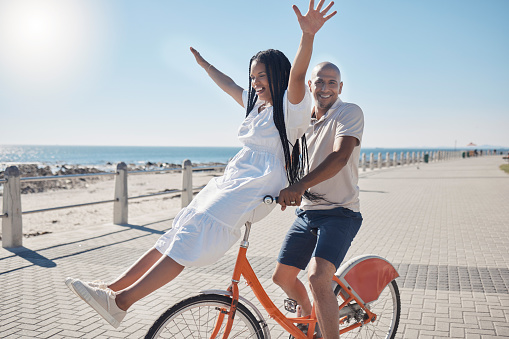 Bicycle, beach and couple with freedom, travel and summer holiday in city sidewalk for wellness, love and care in sunshine. Mental health, black woman and cycling partner at ocean on blue sky mockup