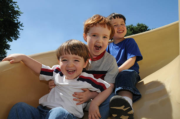 Sliding fun Three brothers have a great time sliding down a spiral slide on a neighborhood schoolyard sliding down stock pictures, royalty-free photos & images