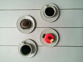 Colorful small fruity cupcakes on small white plates and cups of black coffee on light white background
