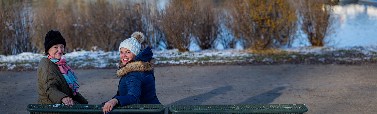Mother and daughter pose while sitting on a bench in Olympia Park in Munich during a cold snowy winter day