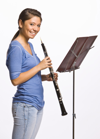 Confident teenage girl playing flute in classroom at high school. Brunette student is practicing woodwind instrument. She is learning music.