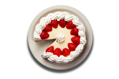 A strawberry cheesecake with a missing slice topped with strawberries and icing photographed from directly above isolated on a white background.