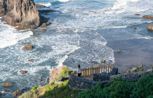 istock A young tourist with her back turned down some stairs onto a beautiful black sand beach. Benijo Beach, Tenerife 1468948049