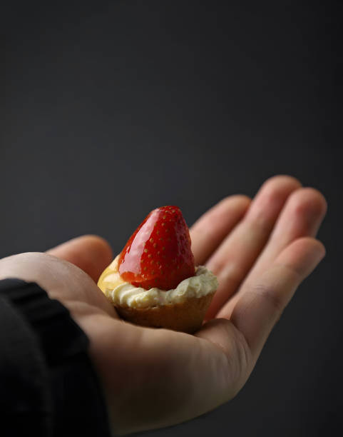 Mini tart in hand, studio shot, selective focus, gray background.