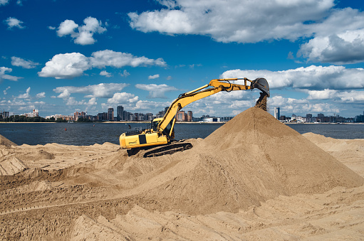 Excavator on the bank of the river in the city digs the sand of the beach,