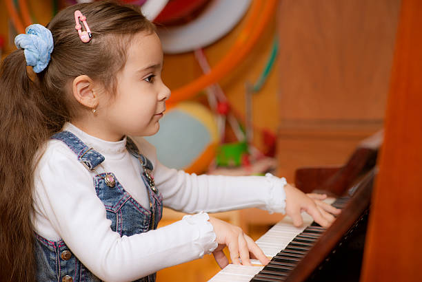Little girl plays piano Small dark-haired girl plays piano in educational class. girl playing piano stock pictures, royalty-free photos & images
