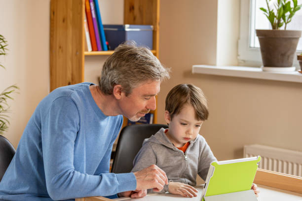 istock 50 year old man helps his 5 year old son with homework using digital tablet 1468965332
