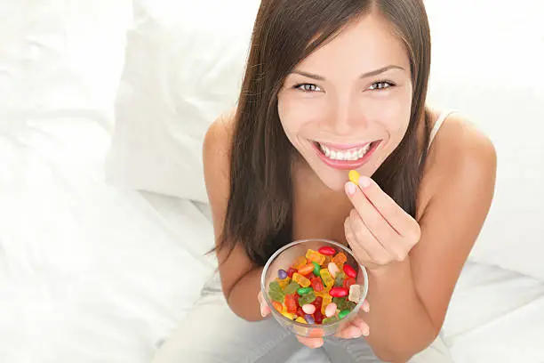 Candy woman eating sweets with a fresh smile in bed - copy space. Top view of Mixed Chinese Asian / Caucasian model. Click for more:
