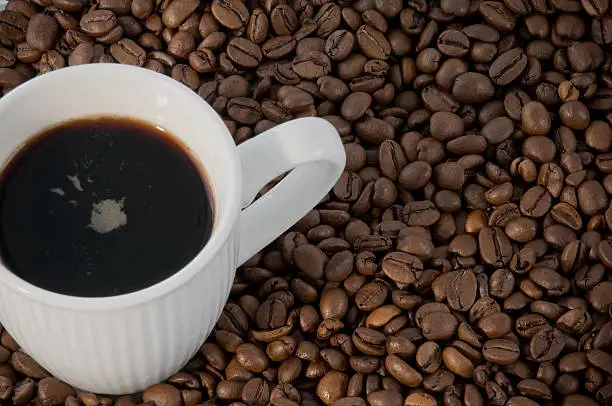White cup of coffee on coffee-beans. Copy space on the lower right.