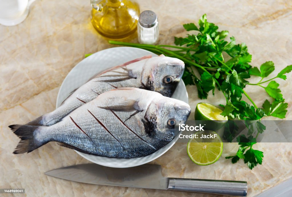 Two raw doradas served on plate with herbs lime salt and oil Two raw gilt-head bream laid on plate with lime parsley salt and oil Appetizer Stock Photo