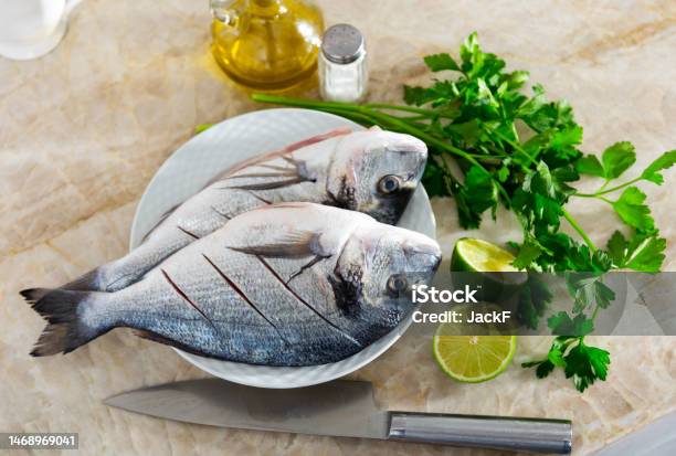 Two Raw Doradas Served On Plate With Herbs Lime Salt And Oil Stock Photo - Download Image Now