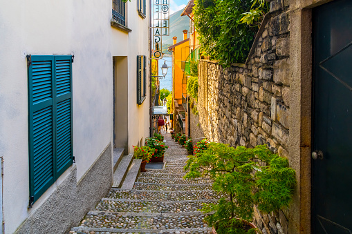 View of the sign and entrance to the Hotel Bellagio, located on a narrow steep staircase alley in the colorful lakefront village of Bellagio, Italy, on Lake Como, Bellagio is a village on a promontory jutting out into Lake Como, in Italy. It’s known for its cobbled lanes, elegant buildings and Villa Serbelloni Park, an 18th-century terraced garden with lake views.