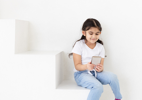 Little girl sitting on stairs, using cell phone