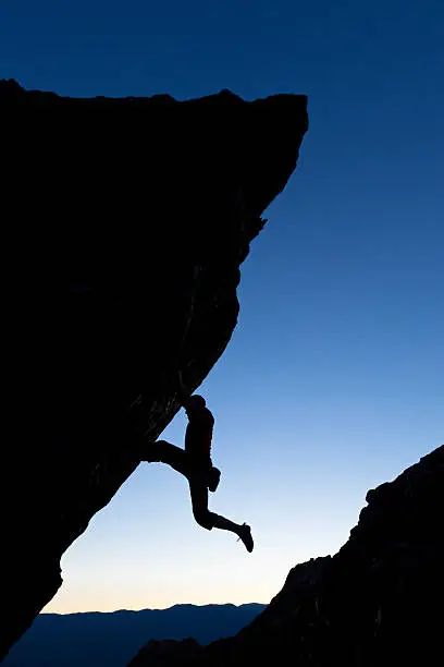 A rock climber ascending a steep boulder at sunset.