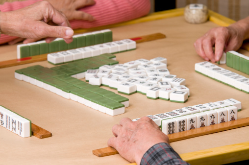 A game of Chinese origin usually played by four persons with tiles resembling dominoes and bearing various designs, which are drawn and discarded until one player wins with a hand of four combinations of three tiles each and a pair of matching tiles.
