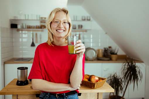 Portrait of a beautiful, young woman making fresh juice of citrus fruit at her kitchen