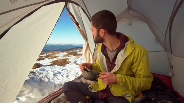 Male hiker enjoys drink in winter shelter
