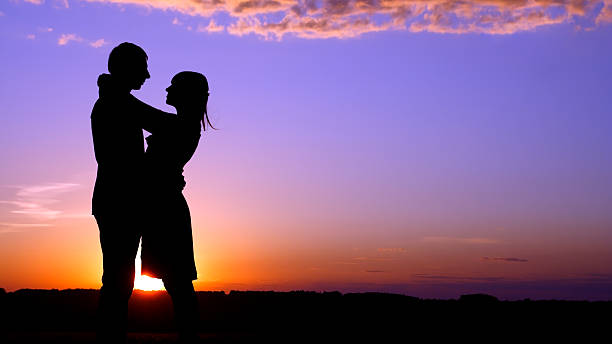 Silhouette of couple embracing with sunset in the background stock photo