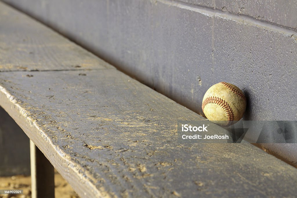 Old Baseball On Dugout Bench An old lone grunge baseball against dugout bench and wall background. Youth Baseball and Softball League Stock Photo