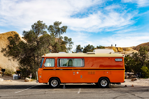 In Joshua Tree National Park, USA a retro RV camper is parked in a lot within a campground on a sunny spring day.
