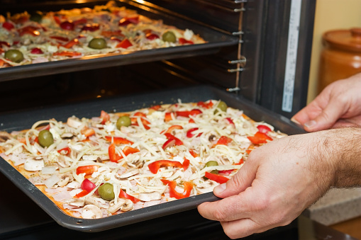 Close-up of male hands taking a  pizza into the oven