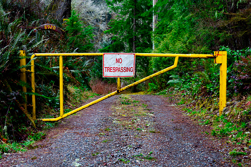 An image of a large metal gate with a red and white no trespassing sign across a gravel roadway.