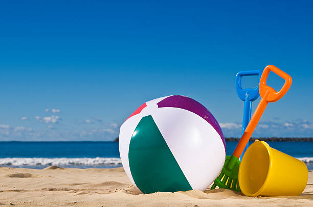 Day at the beach with a beach ball, spade and bucket in the foreground.