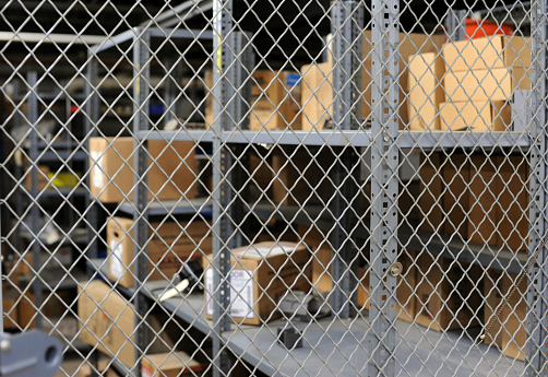 A secure storage area with boxes sitting on shelves behind a chained fence.