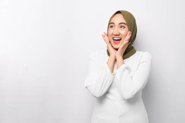 Excited young Asian Muslim woman 20s wearing hijab looking at copy space and raising hands with open mouth, reacting to sale offer isolated on white background. People religious lifestyle concept emocionada joven musulmana asiática de 20 años con hijab mirando el espacio de copia y levantando las manos con la boca abierta, reaccionando a la oferta de venta aislada sobre fondo blanco. concepto de estilo de vida religioso de las personas