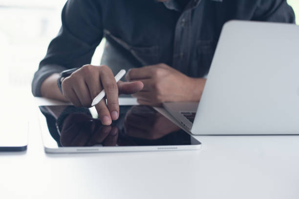 istock Business man finger touching on digital tablet screen while working on laptop computer on office table. Man in casual ware online working, surfing the internet on tablet pc 1469066316