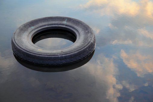 an old tire in water with evening clouds reflecting in it