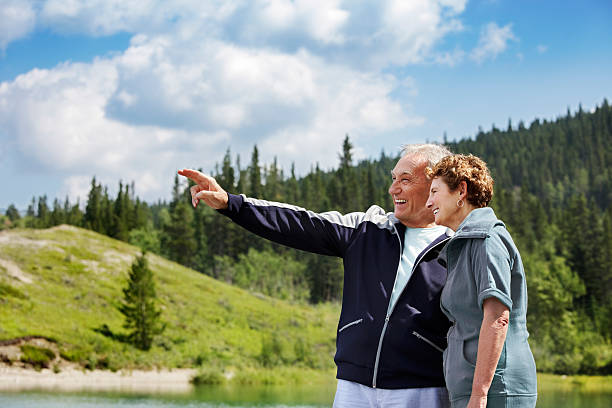 Senior couple pointing and smiling outdoors by a lake stock photo