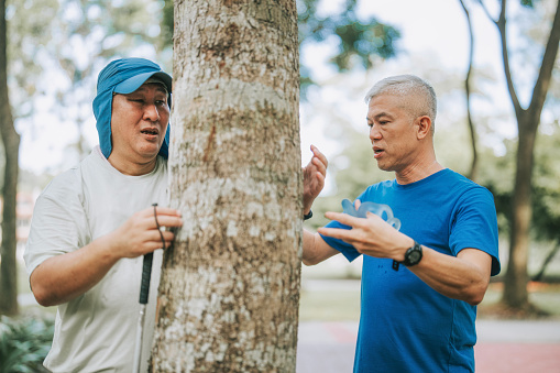 Asian Chinese visually impaired mature man touching and feeling tree trunk in public park during weekend morning