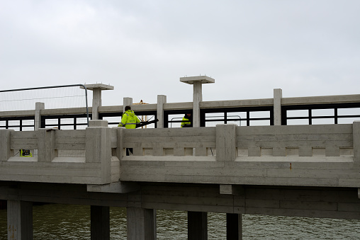 Blankenberge, West-Flanders, Belgium- February 21, 2023: 2 window installers wearing reflective vests work on middle wall on the pier with the placing of black painted covering slats for the windows