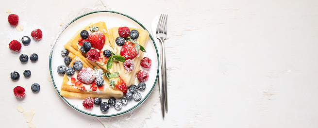 Healthy breakfast, homemade traditional crepes or pancakes with fresh berries, morning light background. Copy space top view, panorama, banner