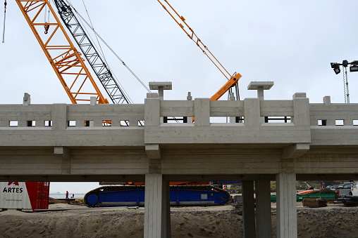Blankenberge, West-Flanders, Belgium - February 21, 2023: yellow excavator crane with blue tracks behind a new rebuild concrete pier in front of a blue sky