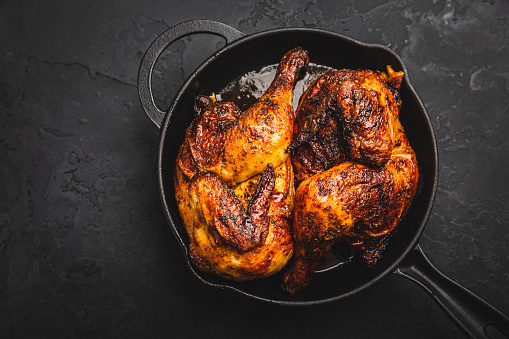 Roasted half chicken in pan on black background
