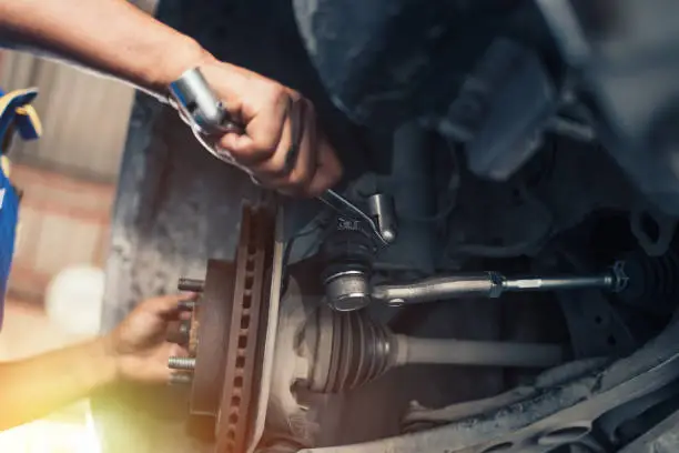 Photo of At a repair shop, a car mechanic tightens the suspension of an elevated vehicle with a spanner.