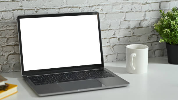 istock Creative workplace with laptop, coffee cup, potted plant and book on white table against brick wall. 1469093892