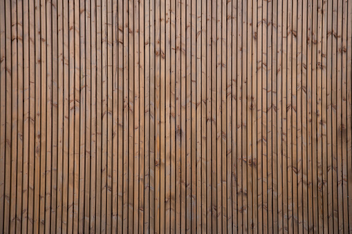 brown natural wooden background with wall of small vertical wood boards on a horizontal facade